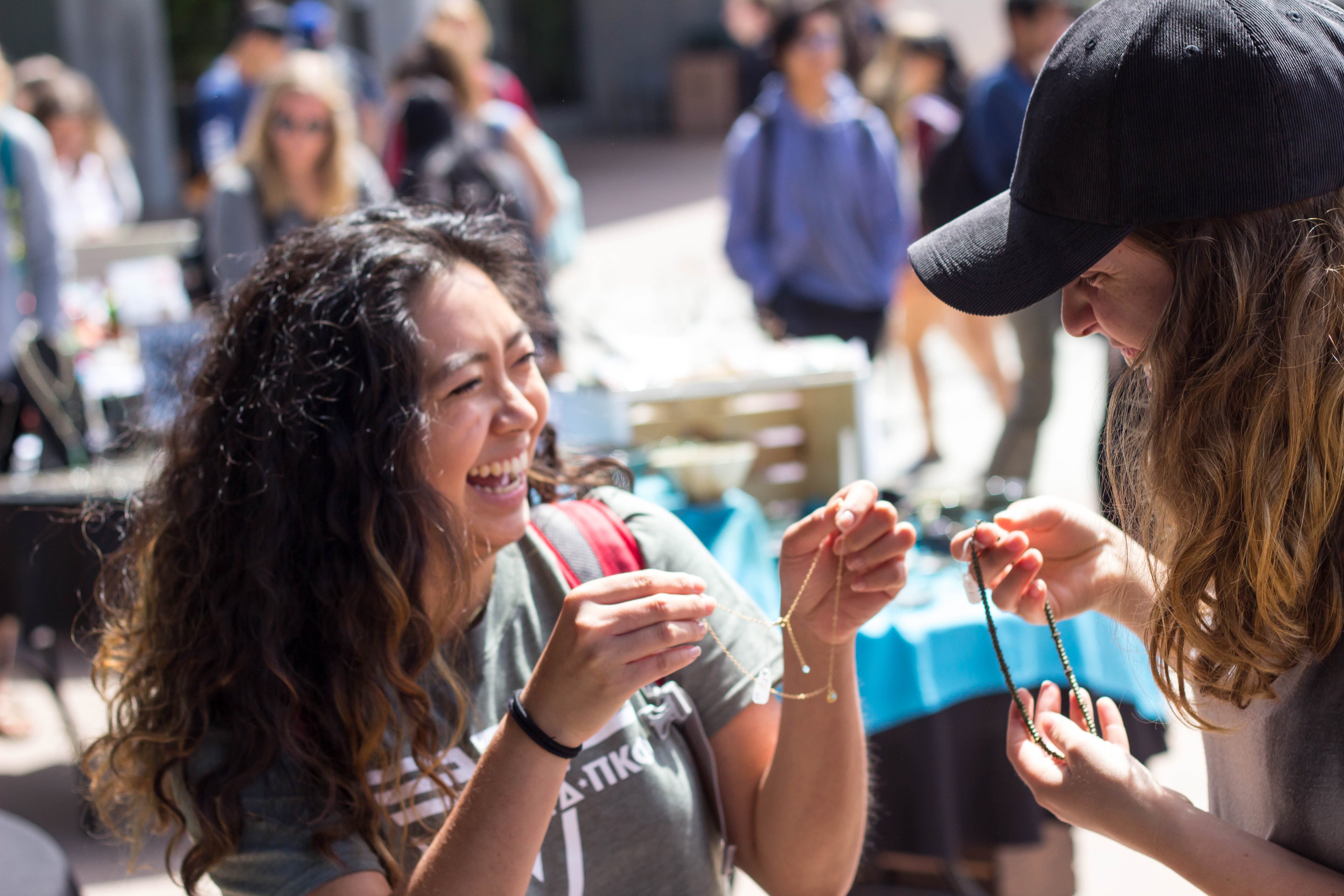 Two female students smile while holding up necklaces at the Craft Sale